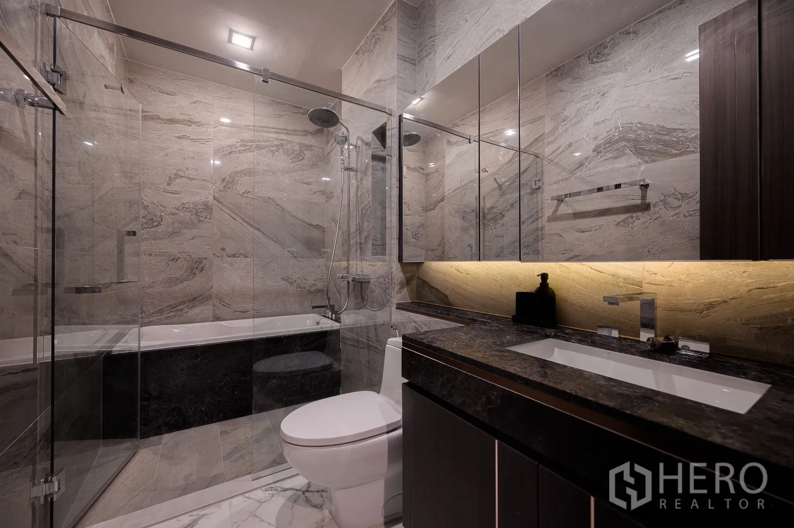 Condominium for rent or sale in Watthana, Bangkok - Luxurious bathroom with marble tiles, glass shower enclosure, bathtub and stone-topped vanity.