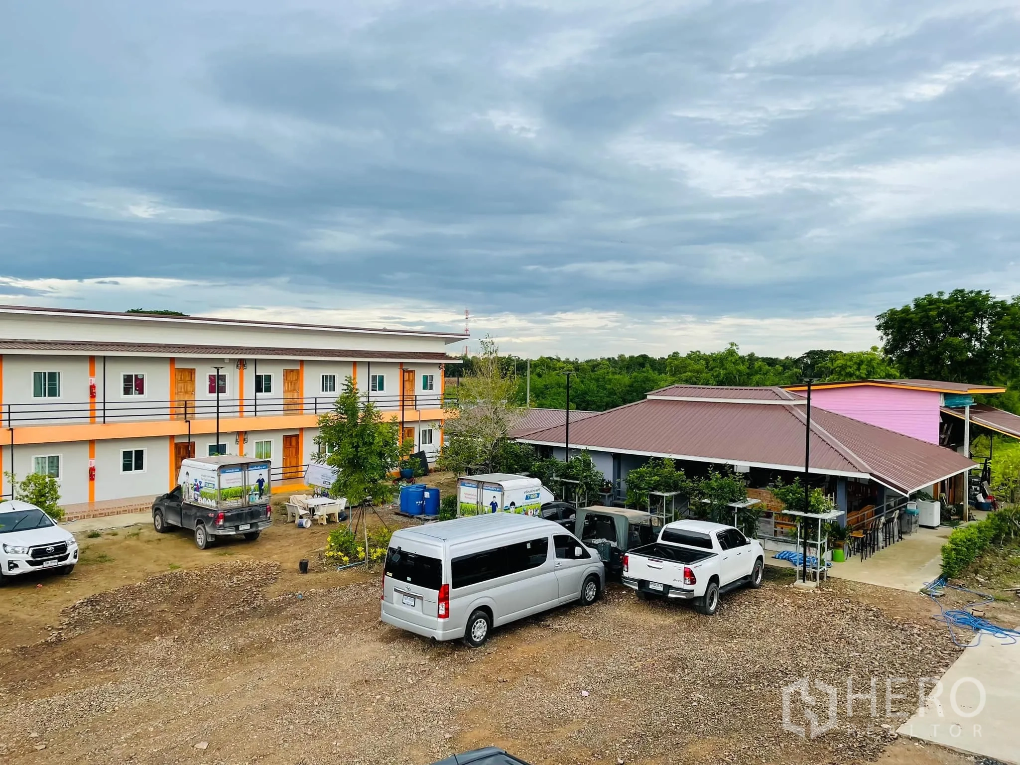 Warehouse for rent or sale in Pathum Thani - Parking and circulation area with vans and pickups beside the apartment building.
