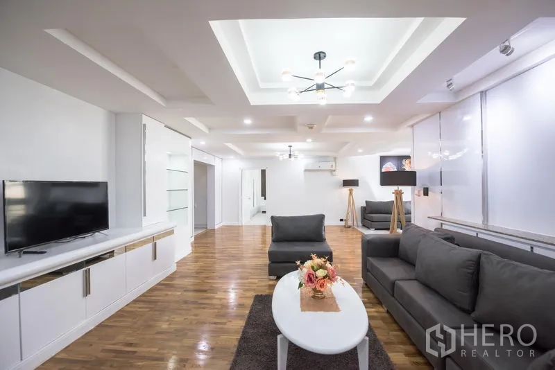 Condominium for rent in Khlong Toei, Bangkok - Living room view with TV console, grey sofas and tray ceilings with recessed lights.
