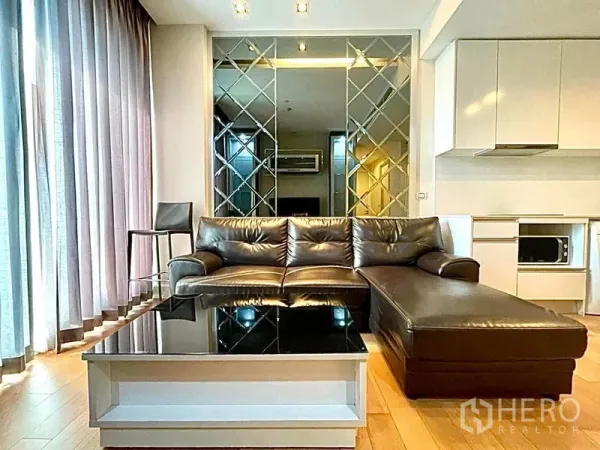 公寓 出租在Chatuchak, Bangkok - 客厅明亮，皮质转角沙发、镜面装饰墙与落地窗帘。