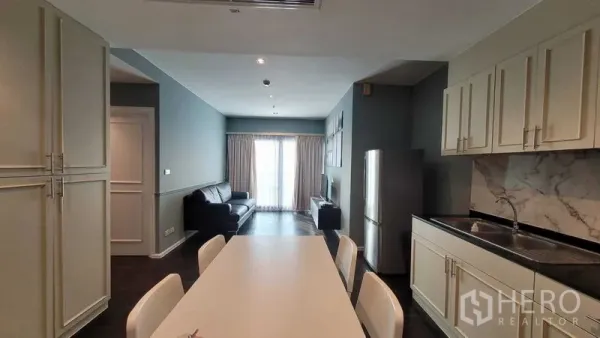 Condominium for rent in Khlong Toei, Bangkok - View from kitchen to living area with sofa, built-in cabinetry and balcony doors bringing natural light.