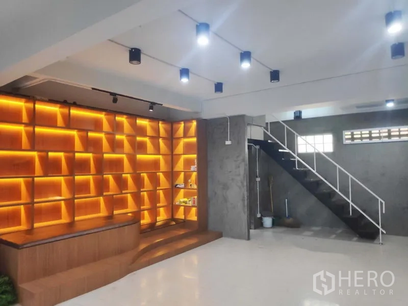 Home Office for rent in Khlong Toei, Bangkok - Feature wall of warm backlit wooden shelving beside an open staircase in a flexible workspace.