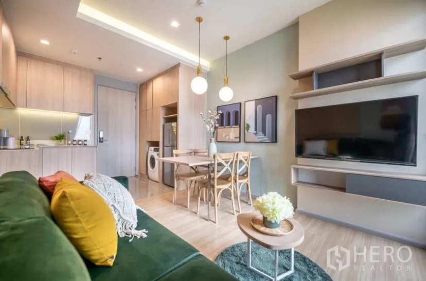 Condominium for rent in Chatuchak, Bangkok - Open-plan lounge with wall-mounted TV, dining set and built-in kitchen cabinetry.