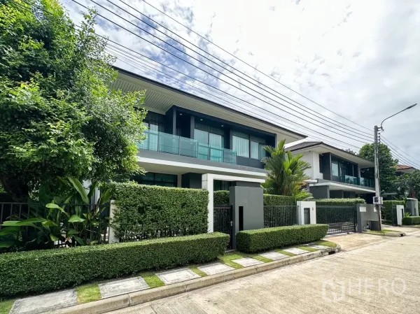 Detached House for rent or sale in Bang Kapi, Bangkok - Street view of an upscale residential row with landscaped hedges and contemporary glass-fronted balconies.