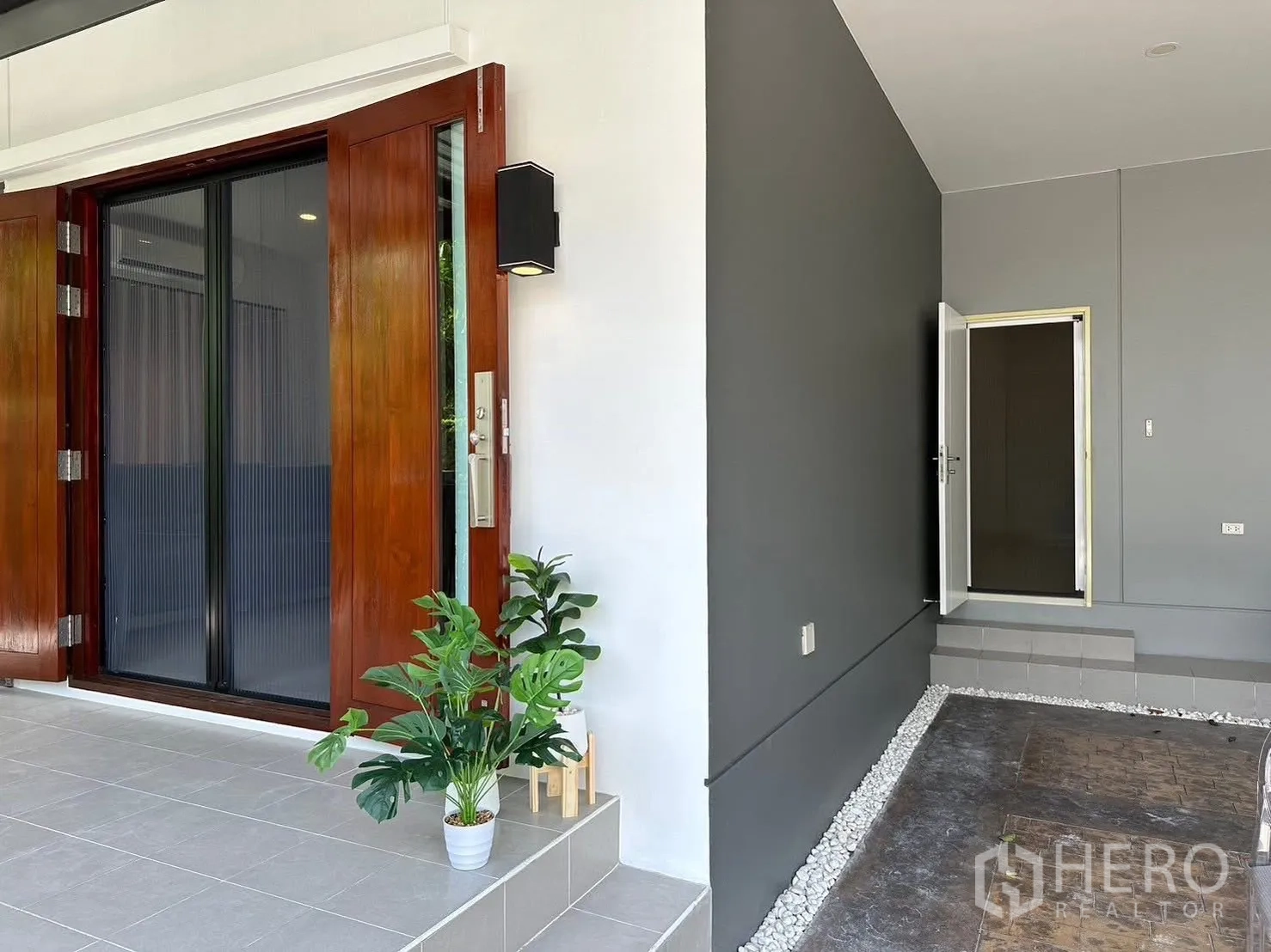 Detached House for rent in Bang Phli, Samut Prakan - Front porch with wooden sliding doors, grey walls and potted greenery.