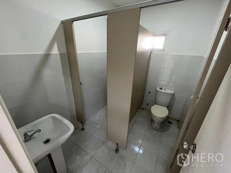 Warehouse for rent or sale in Nonthaburi - Clean restroom with cubicles, sink, and tiled walls and floor.