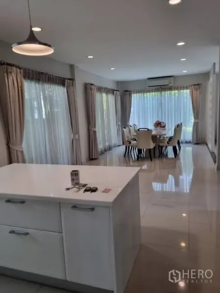 Detached House for rent in Mueang Nonthaburi, Nonthaburi - Bright open-plan space with a white kitchen island facing a dining area and full-height windows.