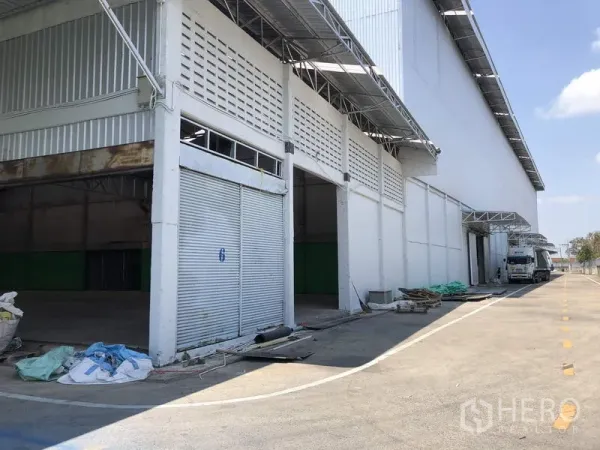 Warehouse for rent in Pathum Thani - Warehouse exterior with multiple roller shutters, covered loading bays, and a wide truck-friendly driveway in Pathum Thani.