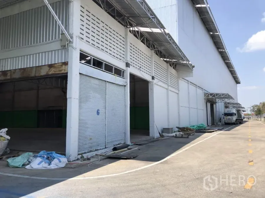 คลังสินค้า ให้เช่าในPathum Thani - ด้านหน้าโกดังมีประตูม้วนหลายบาน หลังคากันสาดลานขนถ่ายสินค้า และถนนกว้างรองรับรถบรรทุกในปทุมธานี