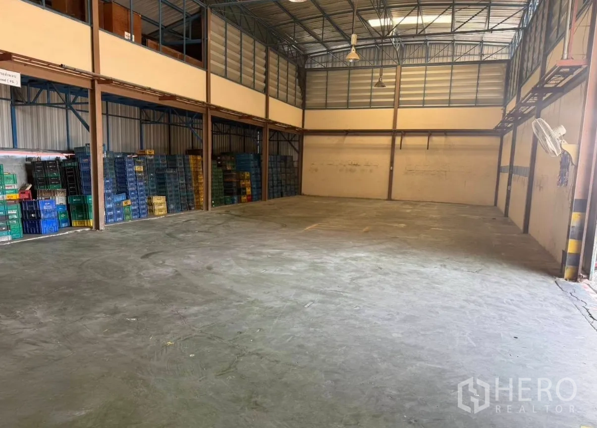 Factory for rent in Bang Phli, Samut Prakan - Storage area with high ceiling and stacked plastic crates along the wall.