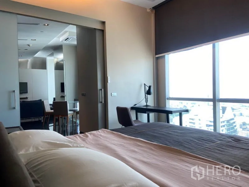 Condominium for rent in Sathon, Bangkok - View from the bedroom toward the living area with a study desk by full-height windows and city views.