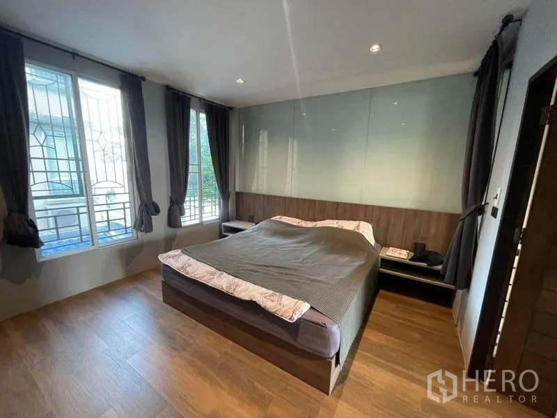 Townhouse for sale in Bang Phli, Samut Prakan - Bedroom with large windows, wood floors, dark curtains and a built-in headboard.