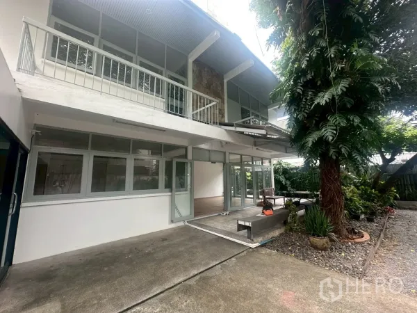 独立式住宅 出租在Watthana, Bangkok - 房屋正面近景，带阳台、落地玻璃门、遮蔽露台与成树。