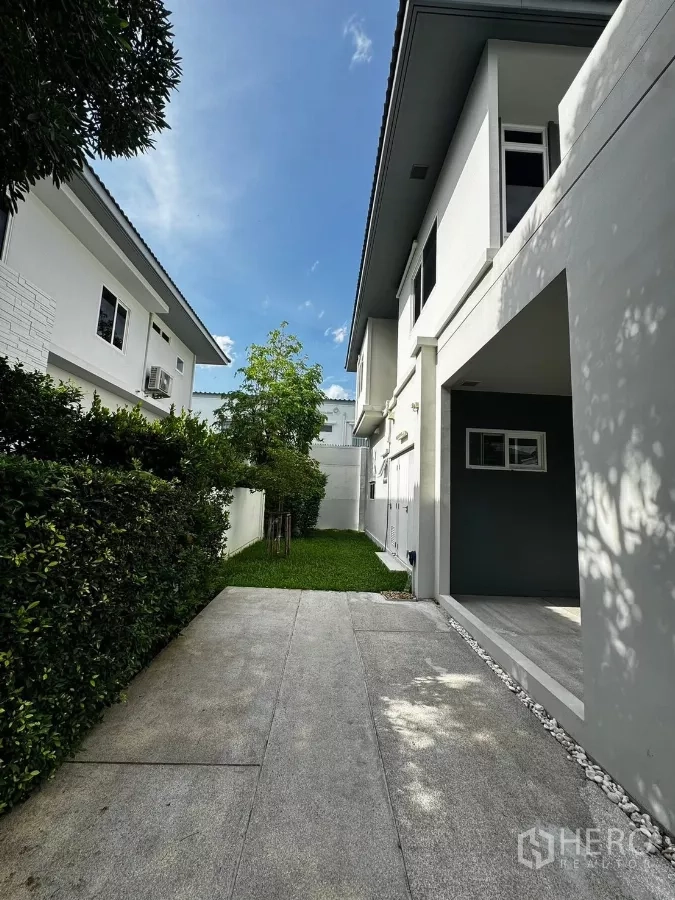 Detached House for rent in Prawet, Bangkok - Wide driveway and covered parking leading past hedges to the side garden.