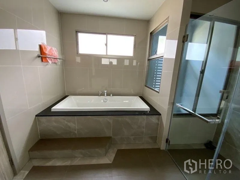 Townhouse for rent in Prawet, Bangkok - Bathroom with raised built-in bathtub, glass shower and windows.