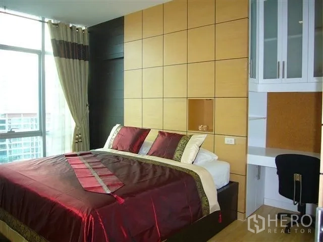 Condominium for rent in Khlong San, Bangkok - Bright bedroom with paneled headboard wall, large bed and corner windows.