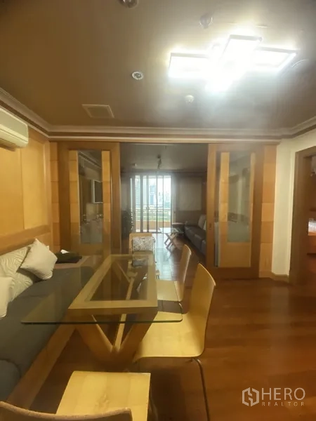 Condominium for rent in Pathum Wan, Bangkok - Dining area with glass table and wooden chairs, wood flooring and sliding doors opening toward the living room and balcony.