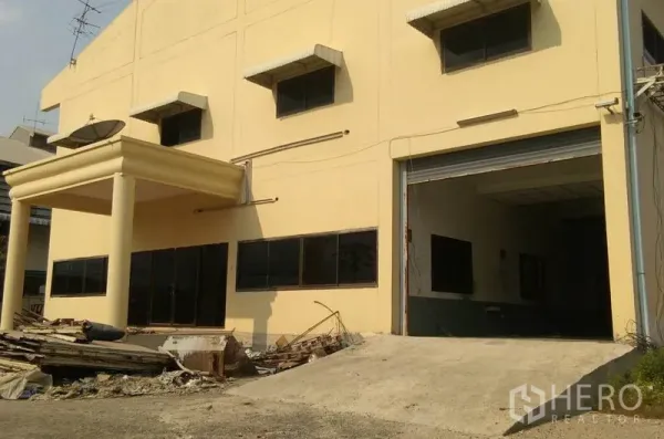 Factory for rent in Bang Phli, Samut Prakan - Two‑storey factory exterior with covered entry, loading ramp and roller shutter door.