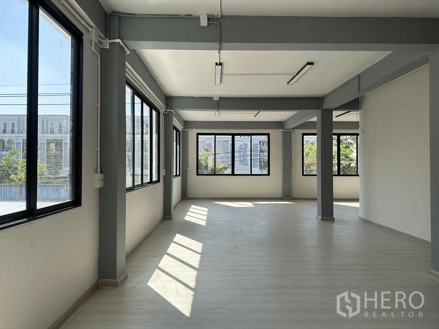 办公空间 出租在Phra Khanong, Bangkok - 采光充足的开放式办公楼层，大片黑框窗、灰色梁与浅色地板。