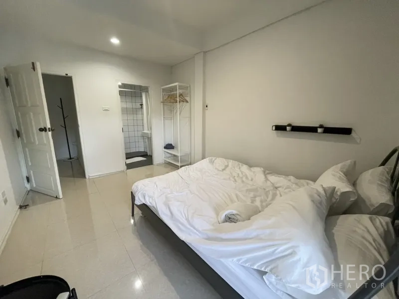 Home Office for rent or sale in Watthana, Bangkok - Bedroom with double bed, open wardrobe and doorway to an en-suite bathroom.