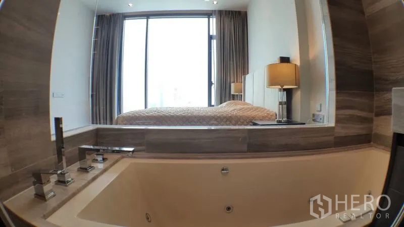 Condominium for rent in Khlong Toei, Bangkok - Luxury bathroom with deep soaking tub and window looking into the bedroom and city light.