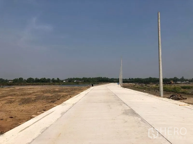 Land for sale in Mueang Samut Sakhon, Samut Sakhon - Wide internal concrete road with utility poles running through cleared land and a distant tree line.