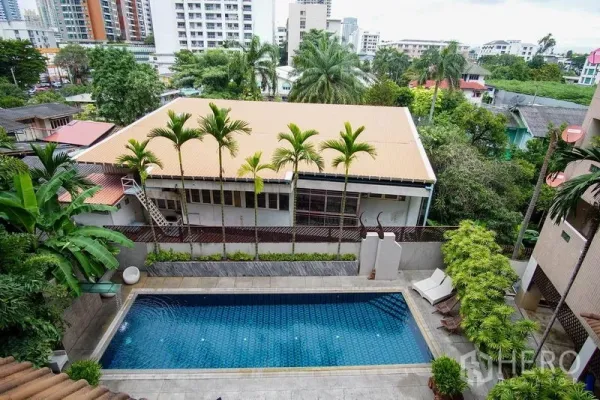Apartment for rent in Watthana, Bangkok - Outdoor swimming pool bordered by palm trees with low-rise cityscape beyond.