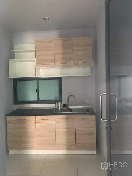 联排别墅 出租或出售在Yan Nawa, Bangkok - 紧凑厨房，浅木色柜体、水槽与小窗，外有玻璃门。