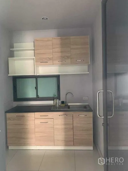 联排别墅 出租或出售在Yan Nawa, Bangkok - 紧凑厨房，浅木色柜体、水槽与小窗，外有玻璃门。