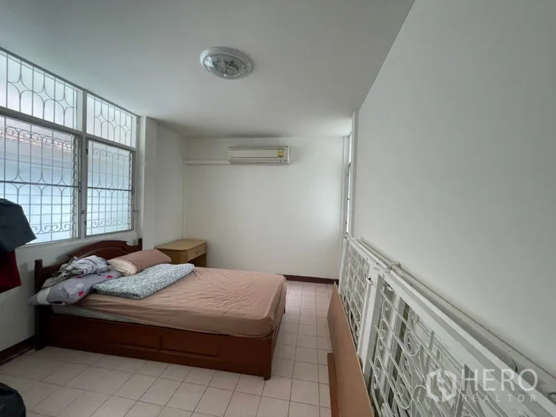 Detached House for rent in Khlong Toei, Bangkok - Compact bedroom with air conditioner, security-grilled windows and wooden bed.