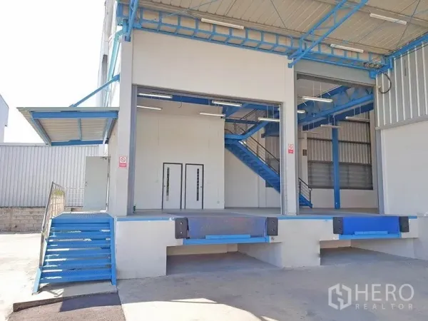 Warehouse for rent in Lat Krabang, Bangkok - Raised loading docks with roller shutters and a blue metal staircase under a canopy at the warehouse entrance.