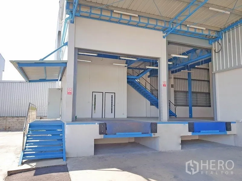 Warehouse for rent in Lat Krabang, Bangkok - Raised loading docks with roller shutters and a blue metal staircase under a canopy at the warehouse entrance.