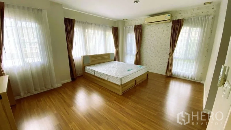 Detached House for rent in Bang Kapi, Bangkok - Spacious master bedroom with bed, multiple windows and wood floors.