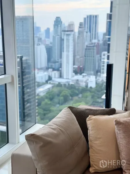 公寓 出租在Pathum Wan, Bangkok - 落地玻璃旁的沙发，望见市中心大楼与绿地公园。