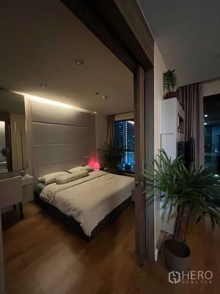 Condominium for rent in Bang Rak, Bangkok - Bedroom opening to the living area with warm lighting and indoor plants.