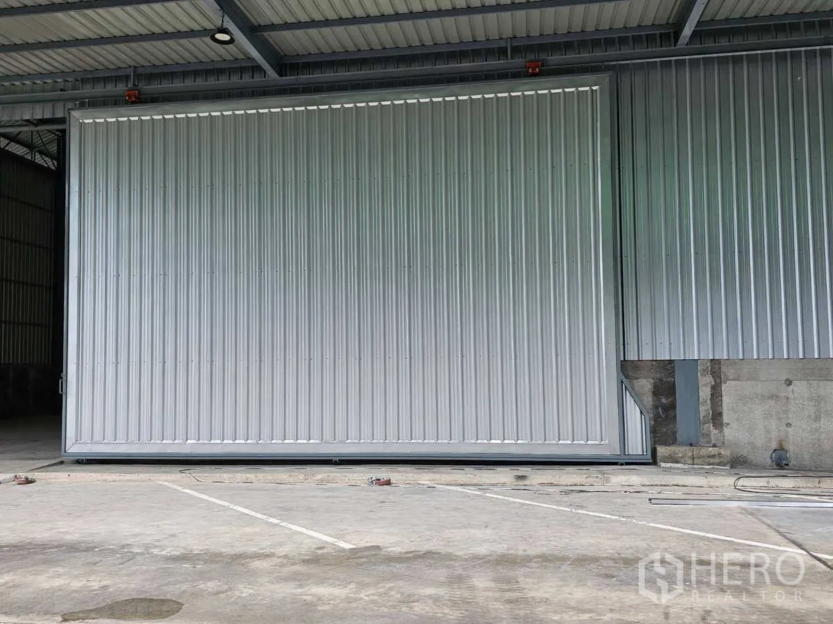 Warehouse for rent in Lam Luk Ka, Pathum Thani - Close view of the oversized gray sliding door at the warehouse entrance.
