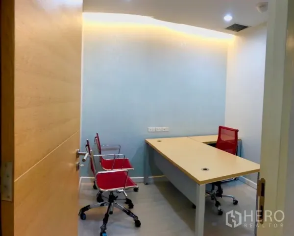 Office Space for rent in Bang Na, Bangkok - Compact manager room with a long worktable, red task chairs and soft cove lighting.