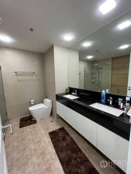 公寓 出售在Pathum Wan, Bangkok - 宽敞卫浴，双洗手台、大镜子、玻璃淋浴间与现代洁具。