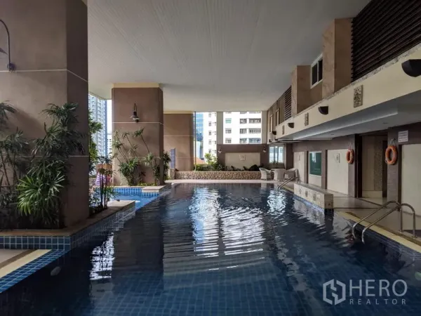 公寓 出租在Watthana, Bangkok - 高层公寓的室内覆盖泳池，蓝色瓷砖池畔与城市景致。