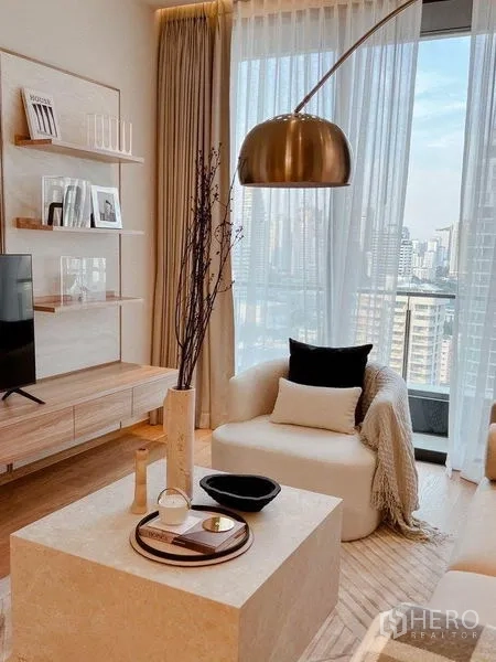 Condominium for rent or sale in Khlong Toei, Bangkok - Bright lounge corner with armchair, arched floor lamp and city view through a full-height window.