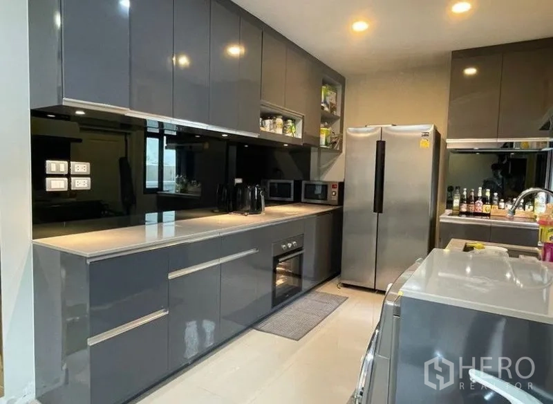 Detached House for rent - Sleek galley kitchen with glossy gray cabinets, built-in oven, microwave, and double-door fridge.