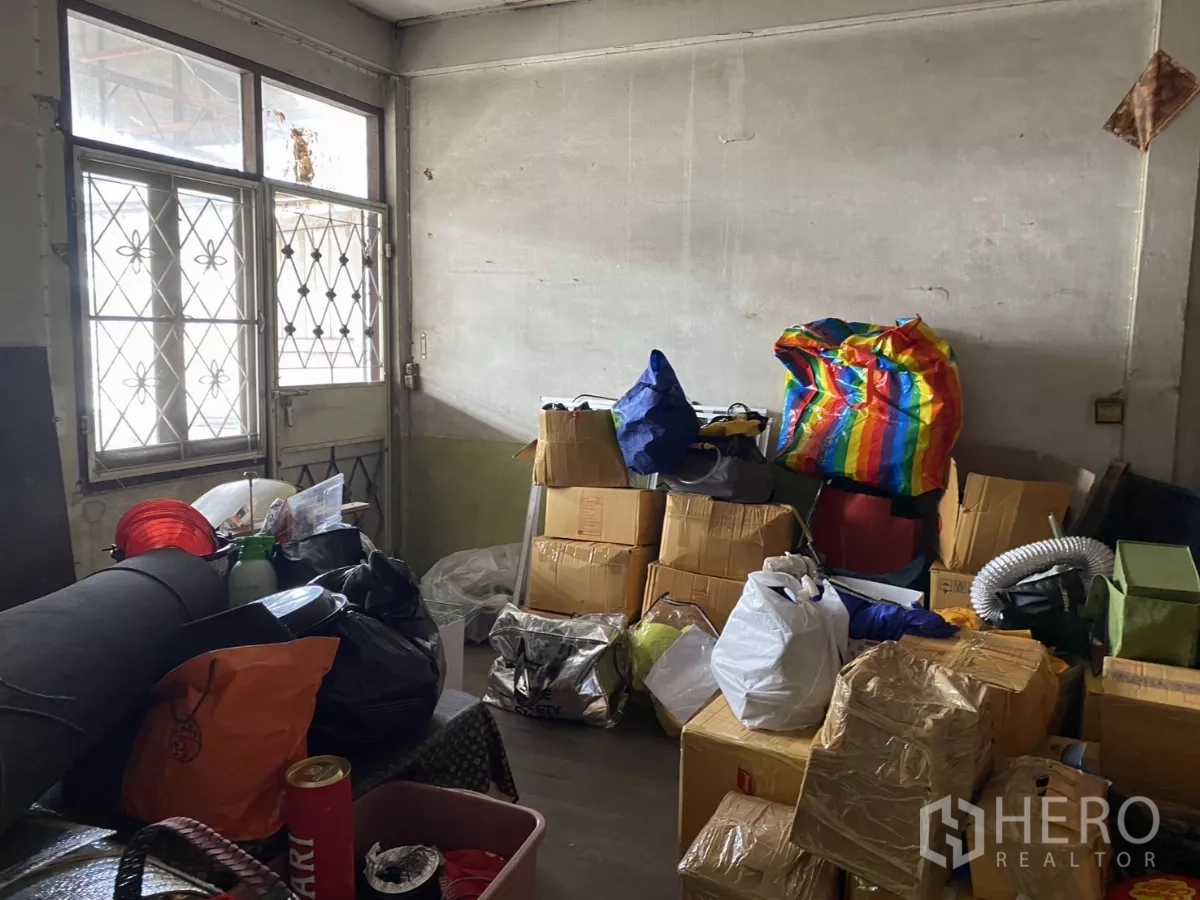 Shophouse for rent in Khlong Toei, Bangkok - Storage room with barred windows filled with boxes and bags.