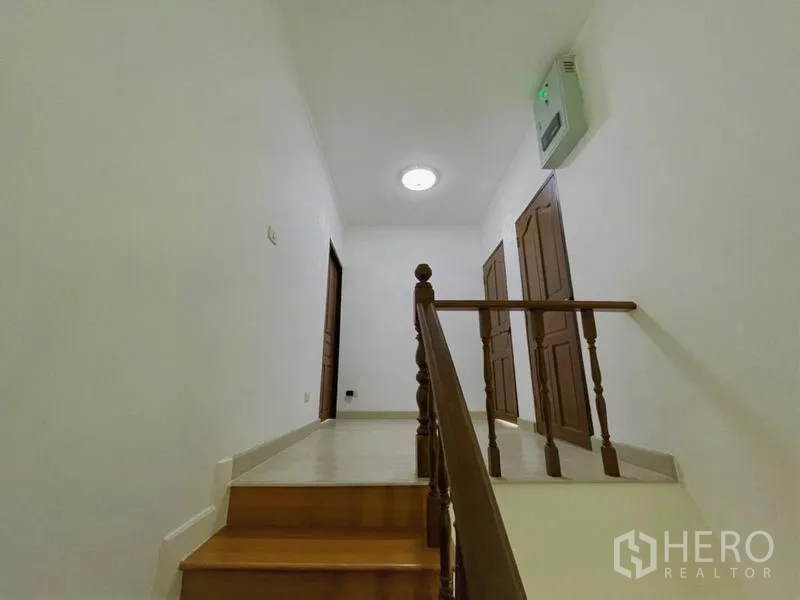 独立式住宅 出租在Suan Luang, Bangkok - 二楼平台，木门通向各卧室，顶灯柔和。
