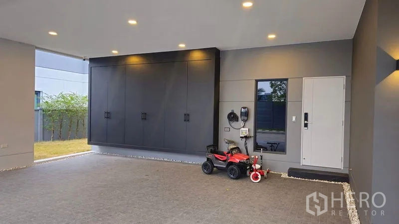 Detached House for sale in Sai Mai, Bangkok - Covered parking area with built-in storage cabinets and recessed lighting at the house.
