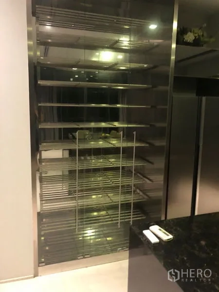 Detached House for rent in Wang Thonglang, Bangkok - Stainless-steel shelving behind glass doors beside a dark stone countertop in the kitchen area.