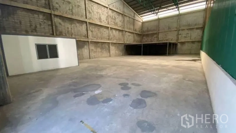 Warehouse for rent in Prawet, Bangkok - Open warehouse floor with tall metal roof, concrete surface, and a mezzanine platform extending across the rear.