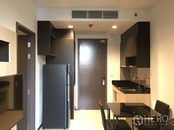 公寓 出租在Watthana, Bangkok - 内置小厨房，黑色台面、水槽、上柜及两人餐桌，位于入户门旁。