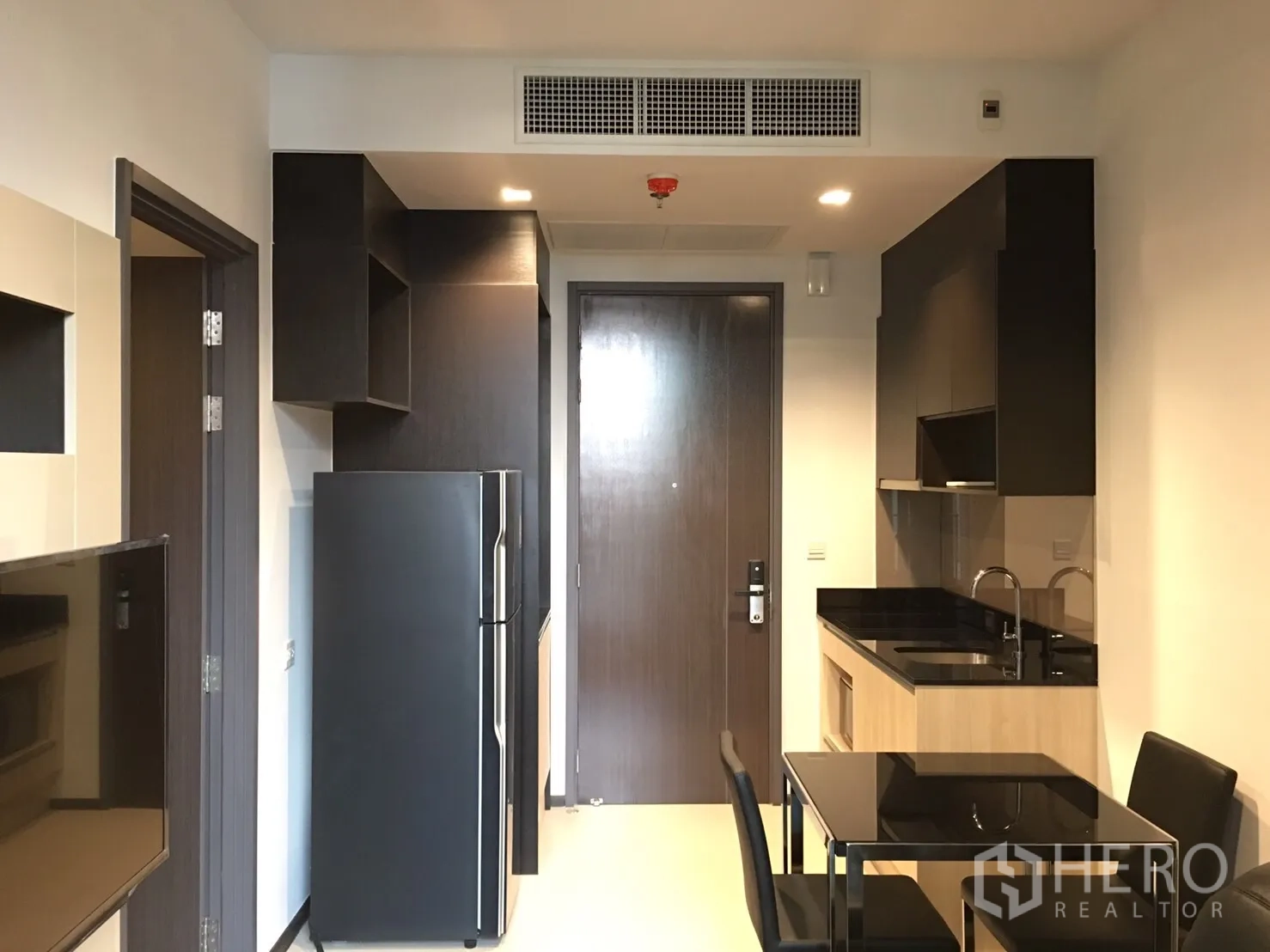 公寓 出租在Watthana, Bangkok - 内置小厨房，黑色台面、水槽、上柜及两人餐桌，位于入户门旁。
