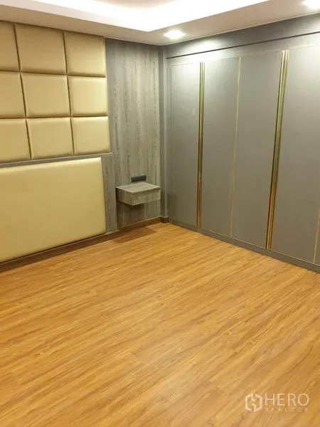 Condominium for rent in Khlong Toei, Bangkok - Bedroom with padded headboard, large wardrobe and warm wood flooring.
