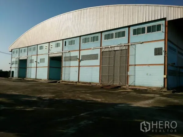 Factory for sale in Lat Lum Kaeo, Pathum Thani - Wide concrete yard facing a high-clearance warehouse with multiple large loading bays and sliding doors.